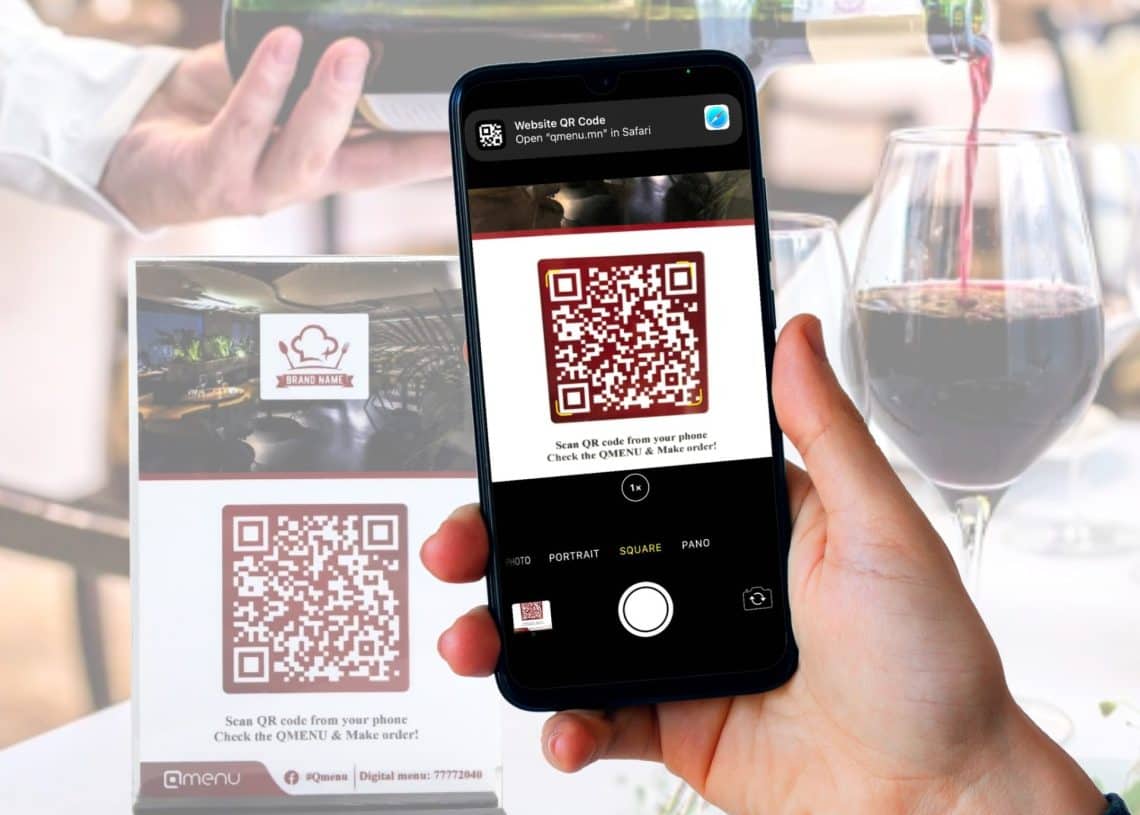 Зоогийн газрын дижитал цэсний тавиураас QR код уншуулж байгаа гар ухаалаг утас барьж байна. Цаана нь хундага лонх дарс асгаж байна. Зургийн дээд талд "QR код уншуул" гэсэн улаан бичвэр байна. Хэрэглэгчийн туршлагыг сайжруулахыг хүссэн аливаа компани эсвэл бизнест тохиромжтой. - Business.MN