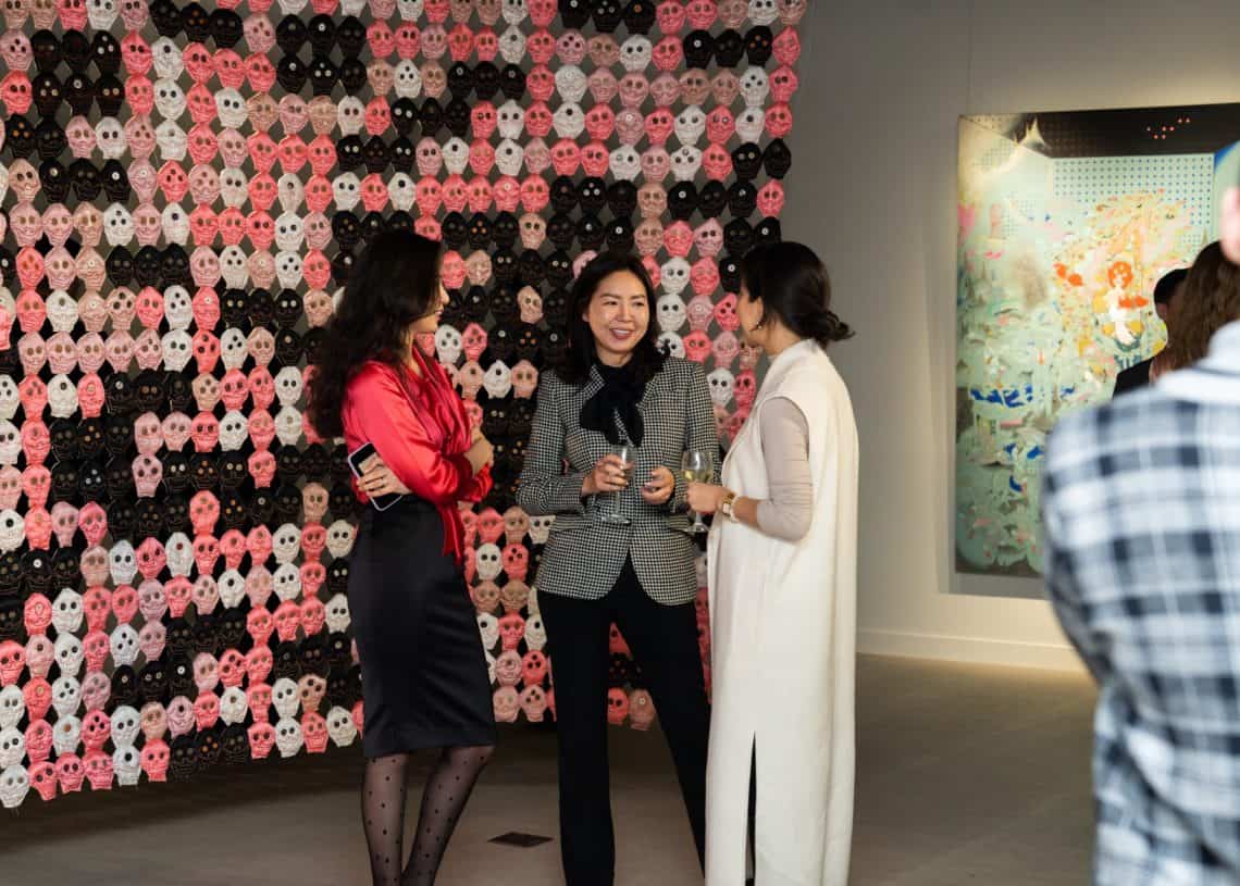 Нэг нь улаан цамц, хар банзал өмссөн, нөгөө нь хар цагаан алаг пиджак өмссөн, гурав дахь нь урт цагаан хантааз өмссөн гурван эмэгтэй урлагийн галерейд гавлын ясны урлагийн инсталляцийн өмнө зогсоод элэгтэй яриа өрнүүлж байна. - Business.MN