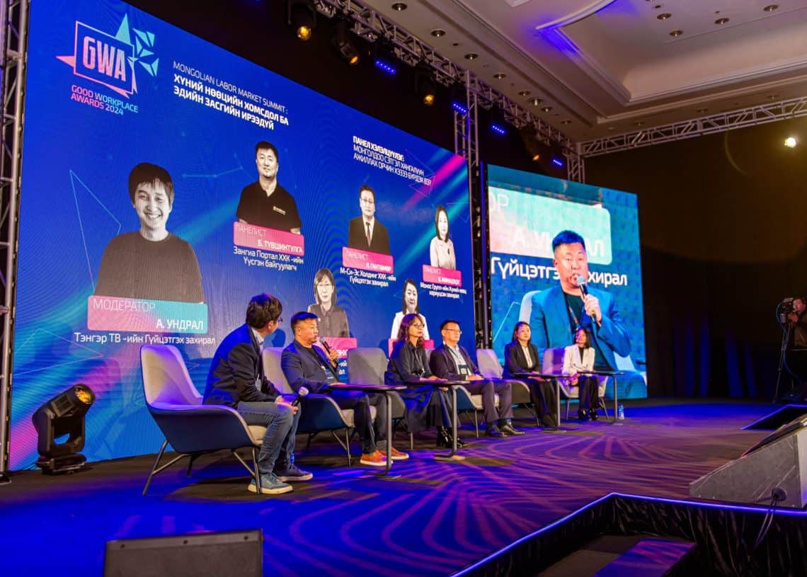 Монголын хөдөлмөрийн зах зээлийн дээд хэмжээний уулзалтын тайзнаа долоон шинжээчийн бүрэлдэхүүнтэй баг оролцож, хүний нөөцийн шинэлэг шийдлүүдийн талаар ярилцаж буй оролцогчдын текст болон зургийг ард нь харуулсан том дэлгэцтэй. Оролцогчид энэхүү динамик форумд идэвхтэй оролцдог. - Business.MN