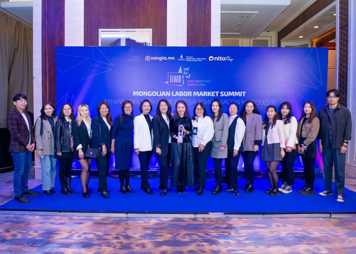 Монголын хөдөлмөрийн зах зээлийн дээд хэмжээний уулзалтын цэнхэр фонны өмнө хэсэг хүмүүс хүний нөөцийн асуудлыг хөндөж байна. Тэд ажил хэргийн хувцас өмсөж, гэр дотор зургаа авахуулж байна. - Business.MN