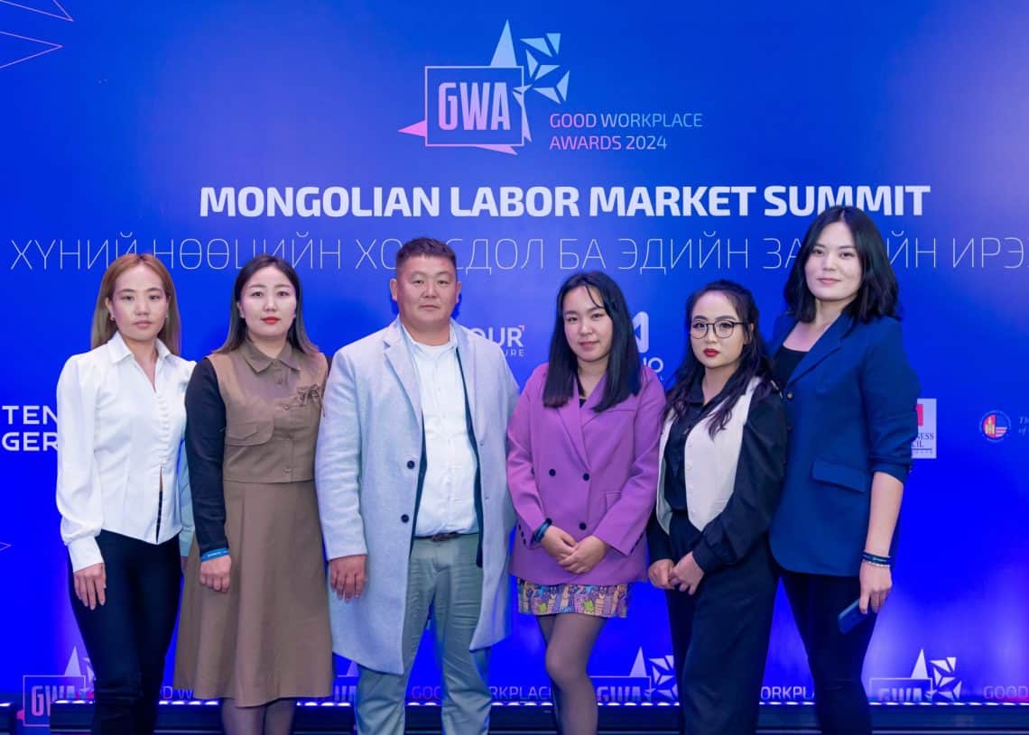 "Монголын хөдөлмөрийн зах зээлийн дээд хэмжээний уулзалт", "Сайн ажлын байрны шагнал 2024" гэсэн бичигтэй цэнхэр фонны өмнө зургаан хүн зогсож байна. Ажил хэрэгч хувцас өмссөн тэд Монголын хөдөлмөрийн зах зээл дэх хүний нөөцийн асуудлыг шийдвэрлэх үүрэг амлалтаа онцолж зургаа авахуулж байна. - Business.MN