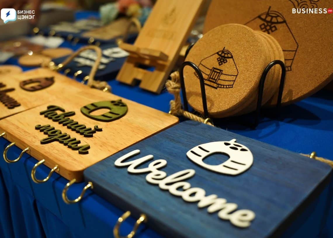 Wooden signs with the word "Welcome" and a Mongolian yurt design are displayed on a blue cloth. Some oval cork coasters are in the background.