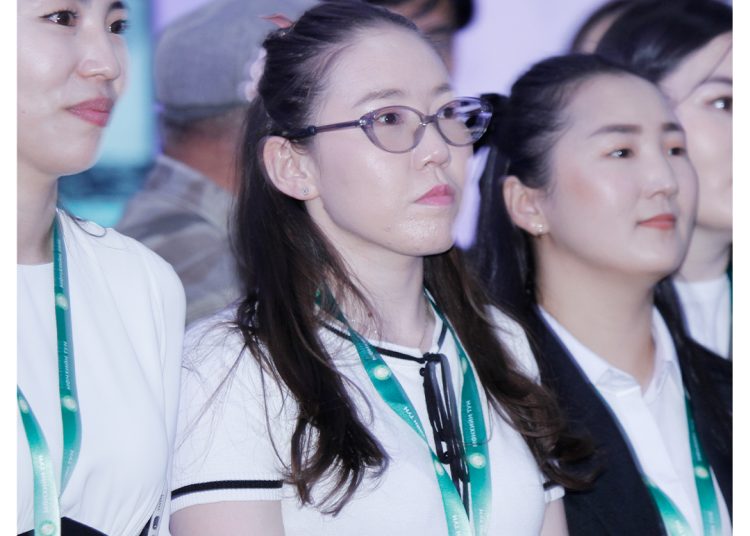 A group of young women wearing ID lanyards stand together indoors, looking attentively ahead. The background is softly blurred, and the MDM Angolle Pharma logo is visible in the top right corner.