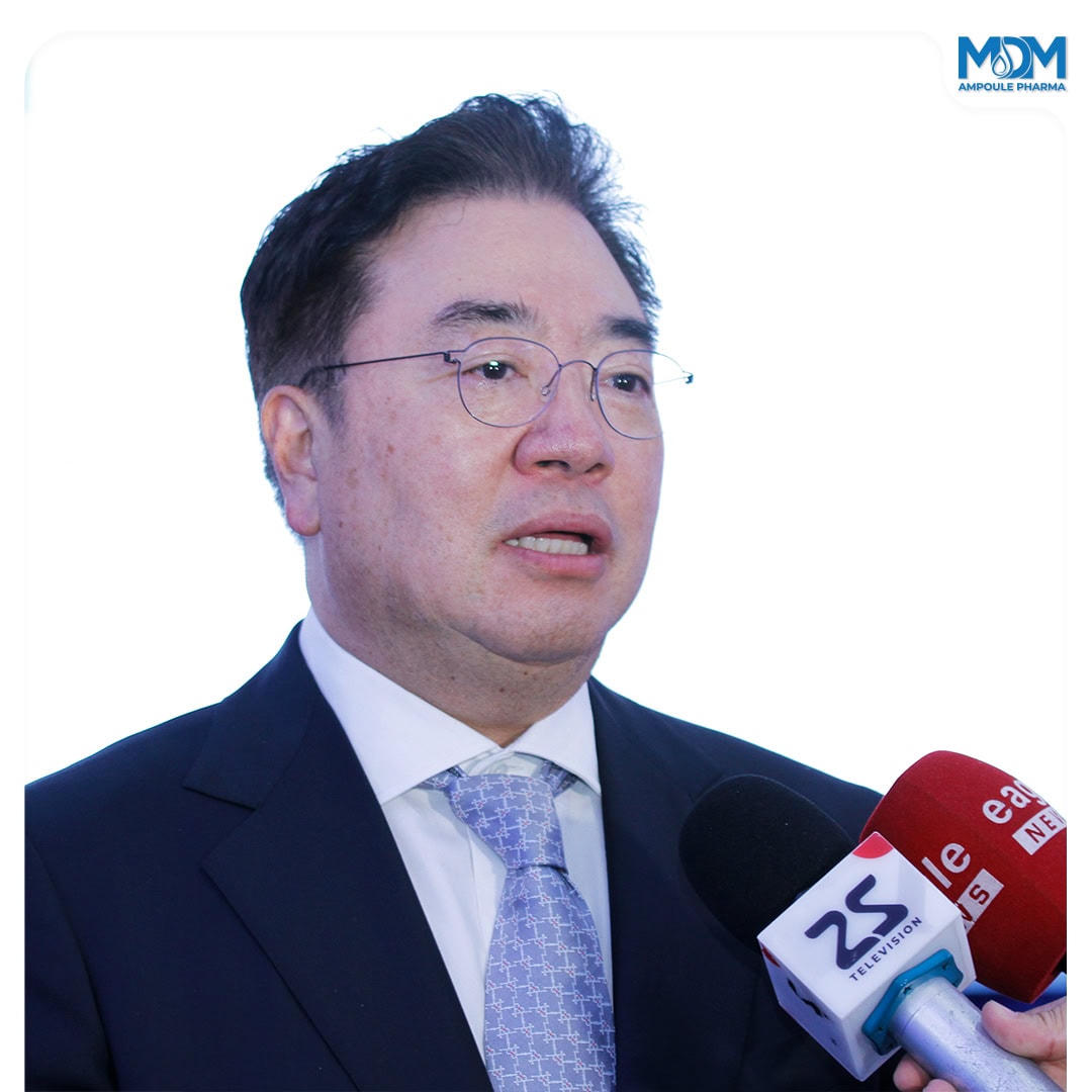 A man in a suit and tie speaks while multiple microphones are held near him. The background is white, and the MDM Ampolle Pharma logo appears in the top right corner.