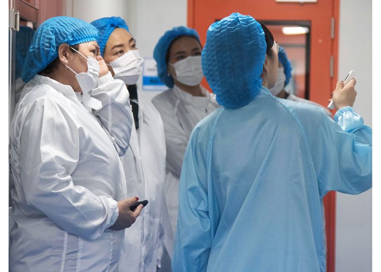 Four people in protective clothing, masks, and hair covers stand in a hallway near a red door. One person gestures while speaking to the others, who are listening attentively. The MDM Ampoule Vietnam logo is visible in the top right corner.