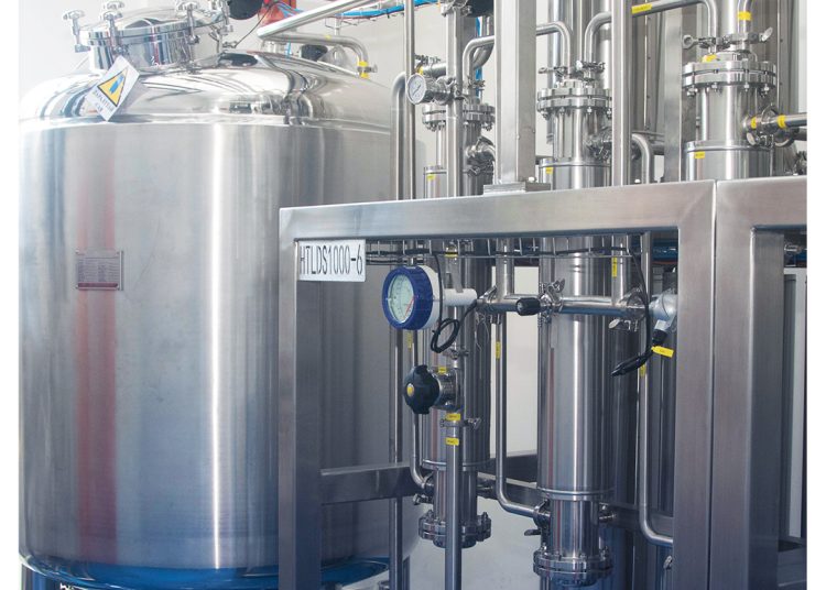 A stainless steel industrial tank and complex piping system in a clean, brightly lit facility, with pressure gauges and valves visible. The MDM ANPOLLE PHARMA logo appears in the top right corner.