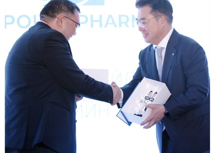 Two men in suits shake hands, one holding a box with vials inside, against a bright, backlit background with the "MOM Ampoule Pharma" logo in the top right corner.