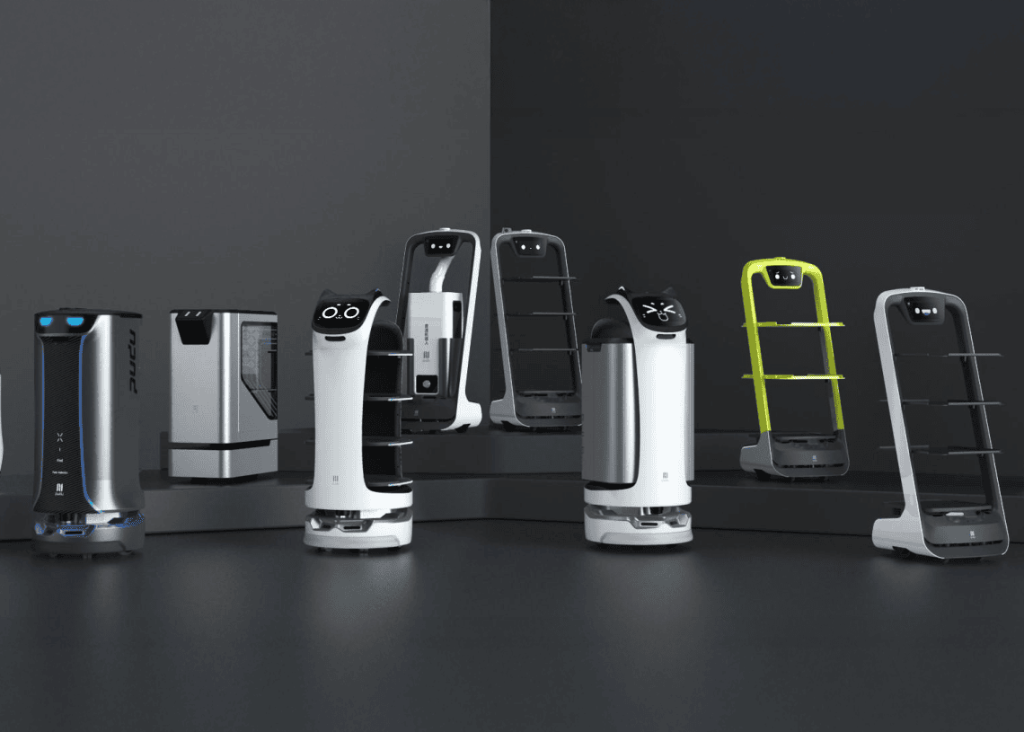 A group of various robots with shelves and digital faces, designed for service or delivery, are displayed on a dark surface against a minimalist background.
