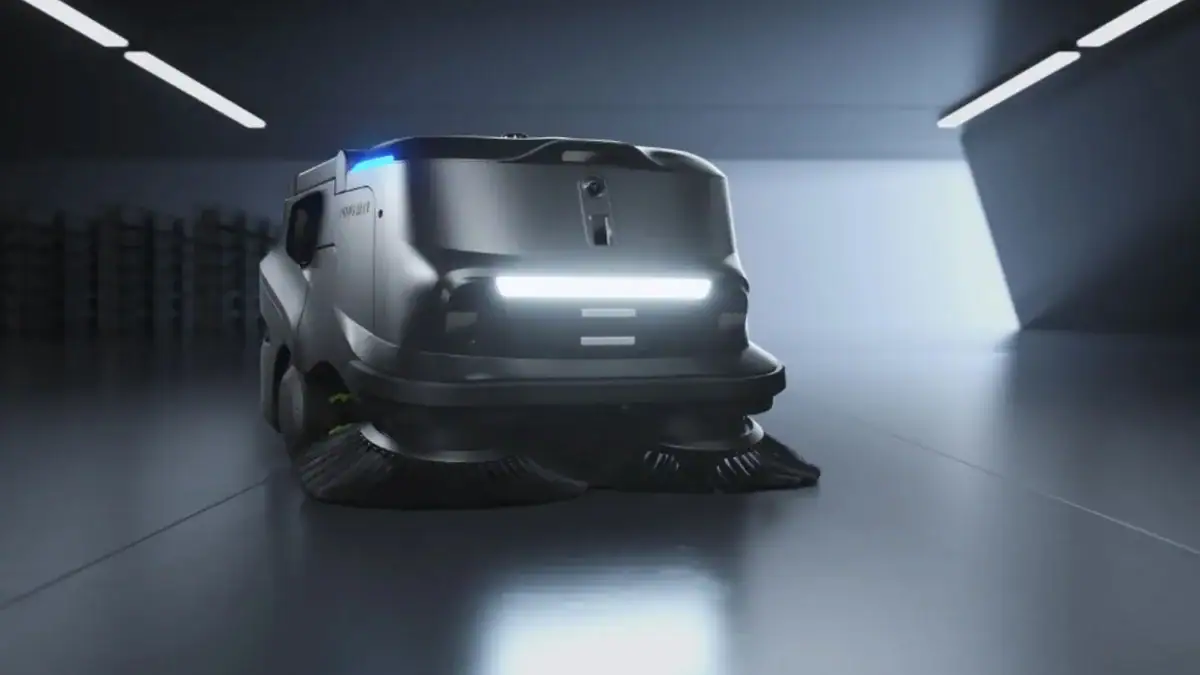 A futuristic, autonomous floor-cleaning robot with headlights and rotating brushes moves across a shiny, modern indoor floor under bright ceiling lights.