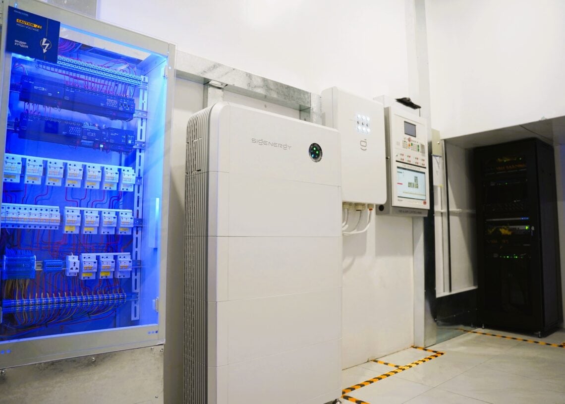 Цахилгаан хавтан, сүлжээний төхөөрөмж, батарей хадгалах төхөөрөмж бүхий цэвэрхэн орчин үеийн серверийн өрөө нь цагаан хана, цайвар хавтантай шалан дээр суурилуулсан ухаалаг барилга байгууламжийн стандартыг тусгасан ногоон байгууламжийг харуулсан зохион байгуулалттай утаснуудыг харуулж байна. - Business.MN