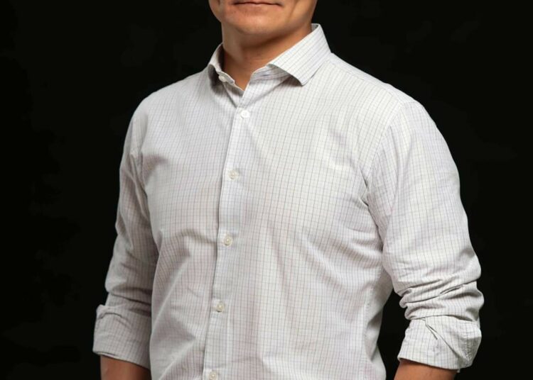 Богино хар үстэй эрэгтэй хар дэвсгэр дээр зогсож, цайвар өнгөтэй, урт ханцуйтай товчтой цамц, шаргал өмд өмссөн байна. Гараа халаасандаа хийгээд үл ялиг инээмсэглэж байгаа нь ногоон ирээдүйн итгэлийг илтгэнэ. - Business.MN