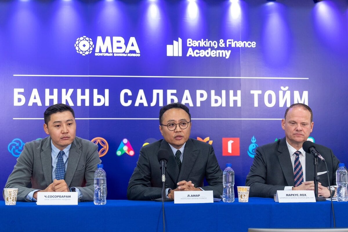 Костюм өмссөн гурван эр микрофон, савтай ус барьсан ширээний ард суугаад хэвлэлийн бага хурал дээр чанаргүй зээлийн талаар ярьж байна. Тэдний ард “Banking & Finance Academy. - Business.MN