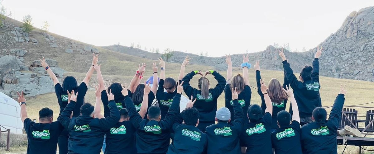 Ар талдаа "Валома"-тай таарч тохирох хар юүдэнтэй цамц өмссөн хэсэг хүмүүс гадаа нуруугаараа камерт тулан, Кетомо Кафе дарсны ойролцоо гараа өргөөд, хадархаг толгод, өвслөг талбайн дунд гэртээ мэт санагддаг. - Business.MN