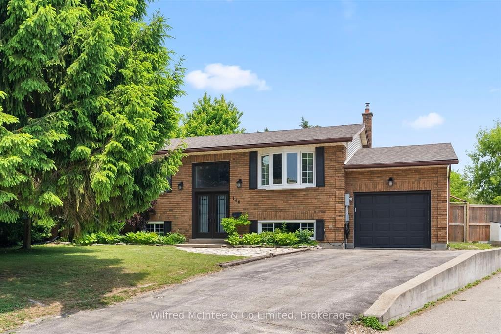 A single-story brick house with a raised entry, attached single-car garage, and a sloped driveway, surrounded by lawn and trees.