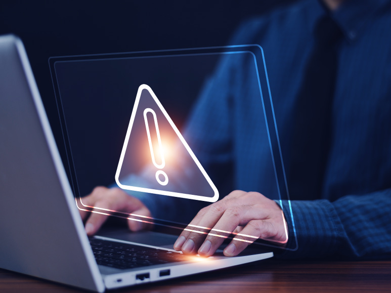 close em uma pessoa usando um notebook enquanto um ícone de perigo aparece sobre a imagem.