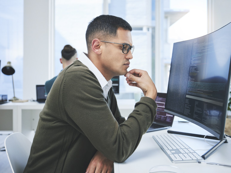 homem sentado em frente a um computador analisa os dados que vê na tela