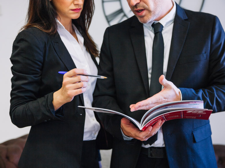 duas pessoas conversam de forma séria enquanto apontam para uma revista que está nas mãos de uma delas representando governança