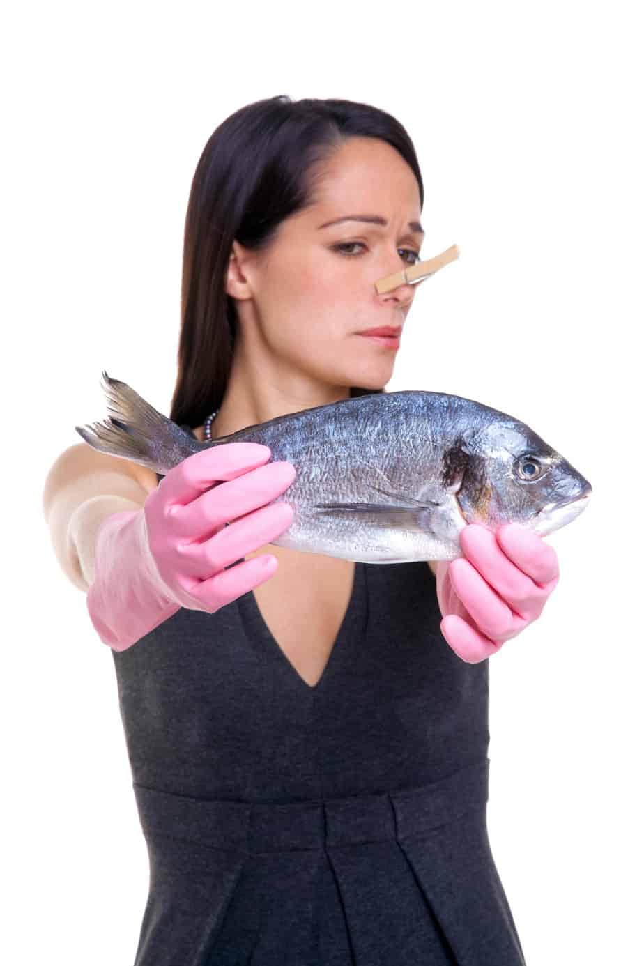 Lady holding a fish with her nose pinched closed with a closepin.