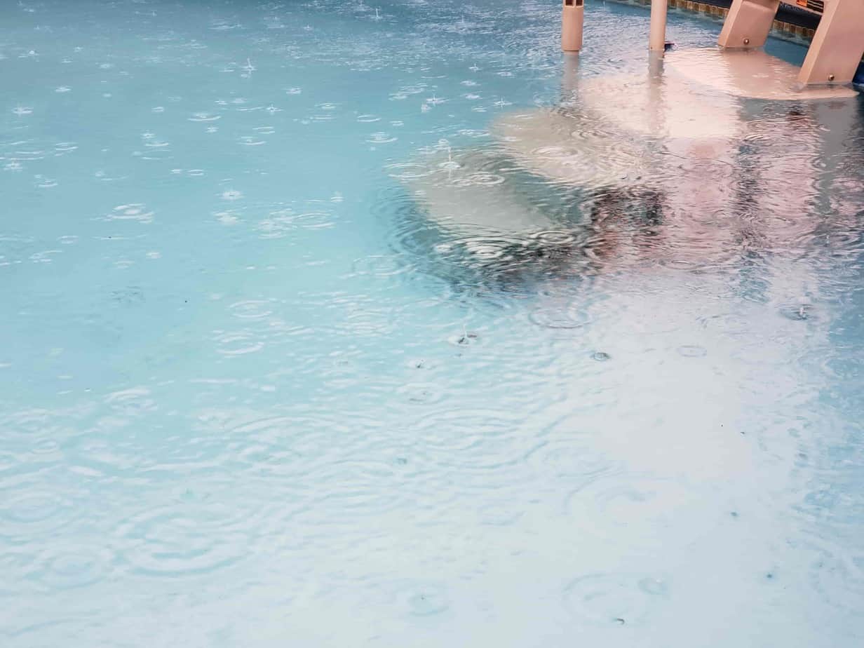 Raindrops falling into the pool water next to the ladder underneath it.
