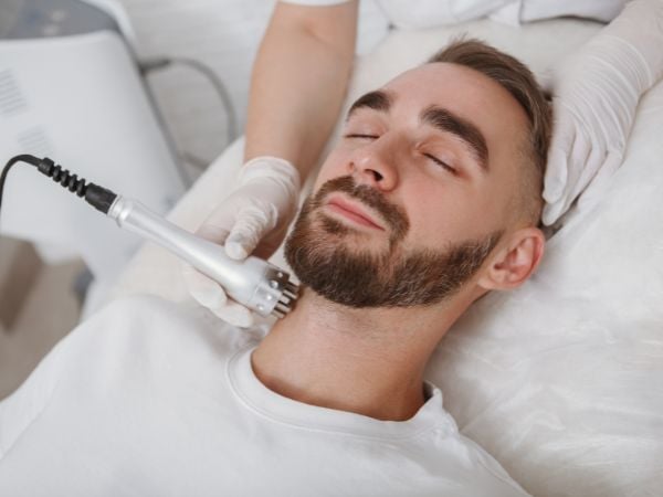 Cosmetóloga atendiendo a un hombre en un tratamiento facial