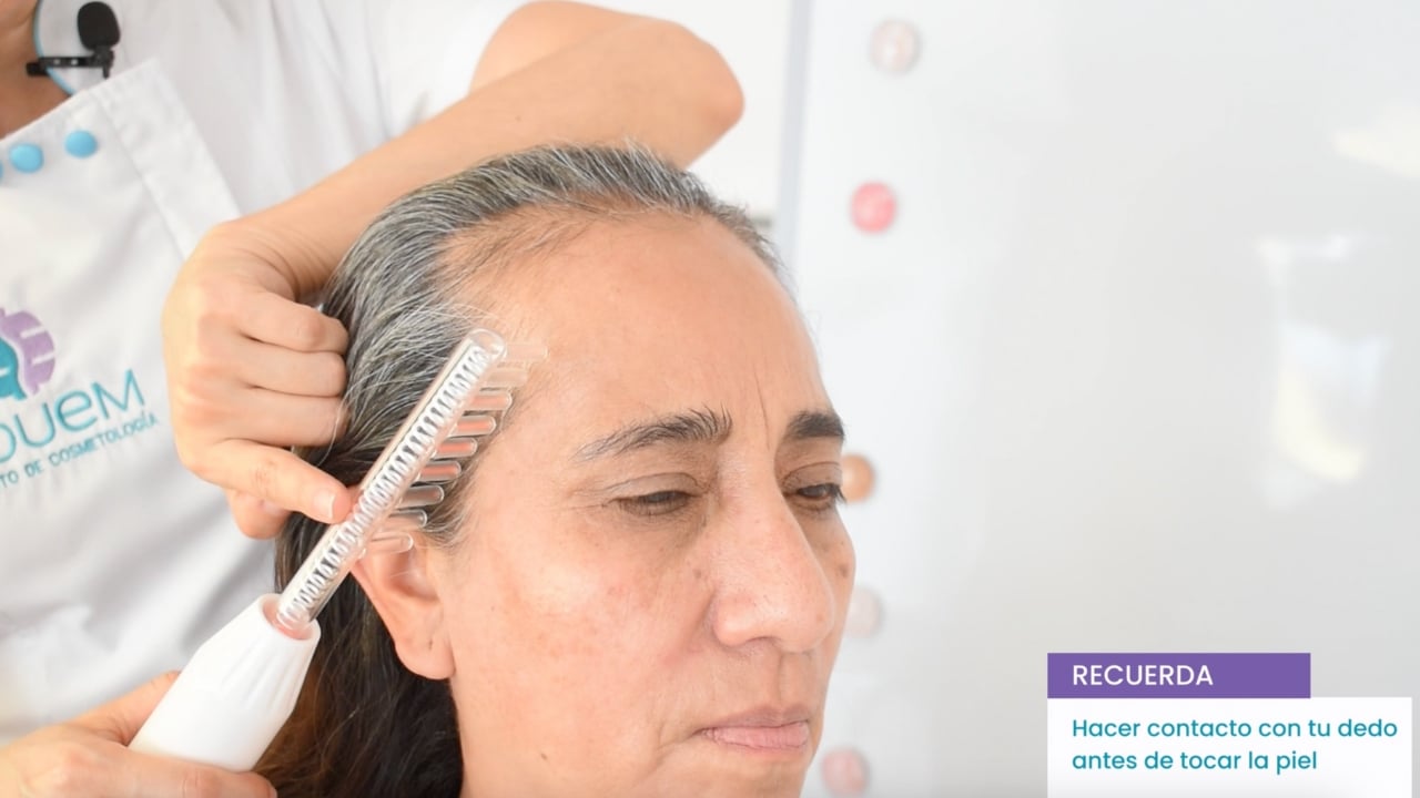 Cosmetóloga aplicando un tratamiento de alta frecuencia en el cuero cabelludo de una clienta.