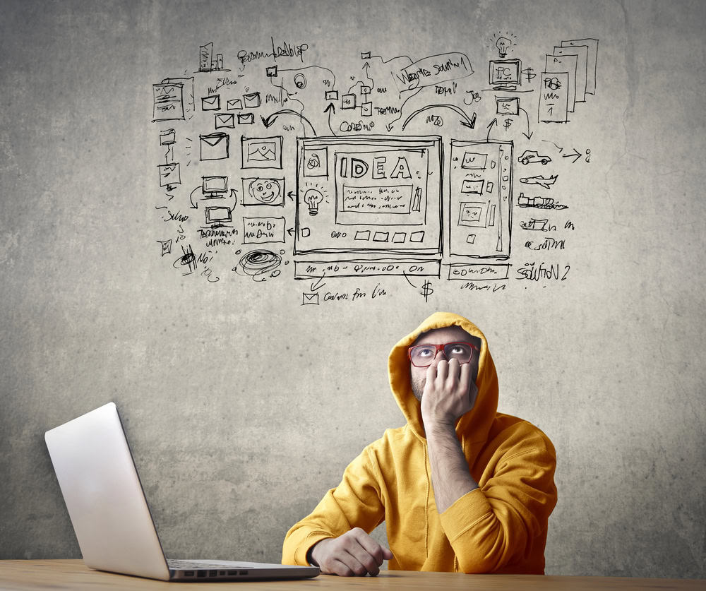 אדם לובש קפוצ'ון צהוב יושב ליד שולחן עבודה עם מחשב נייד, מכסה את פיו ביד. מאחוריהם על הקיר סקיצה מורכבת של תרשימים, גרפים ודיאגרמות עם המילה "IDEA" בולטת במרכז - סיעור מוחות עבור בניית אתר וורדפרס מתקיים בבירור.