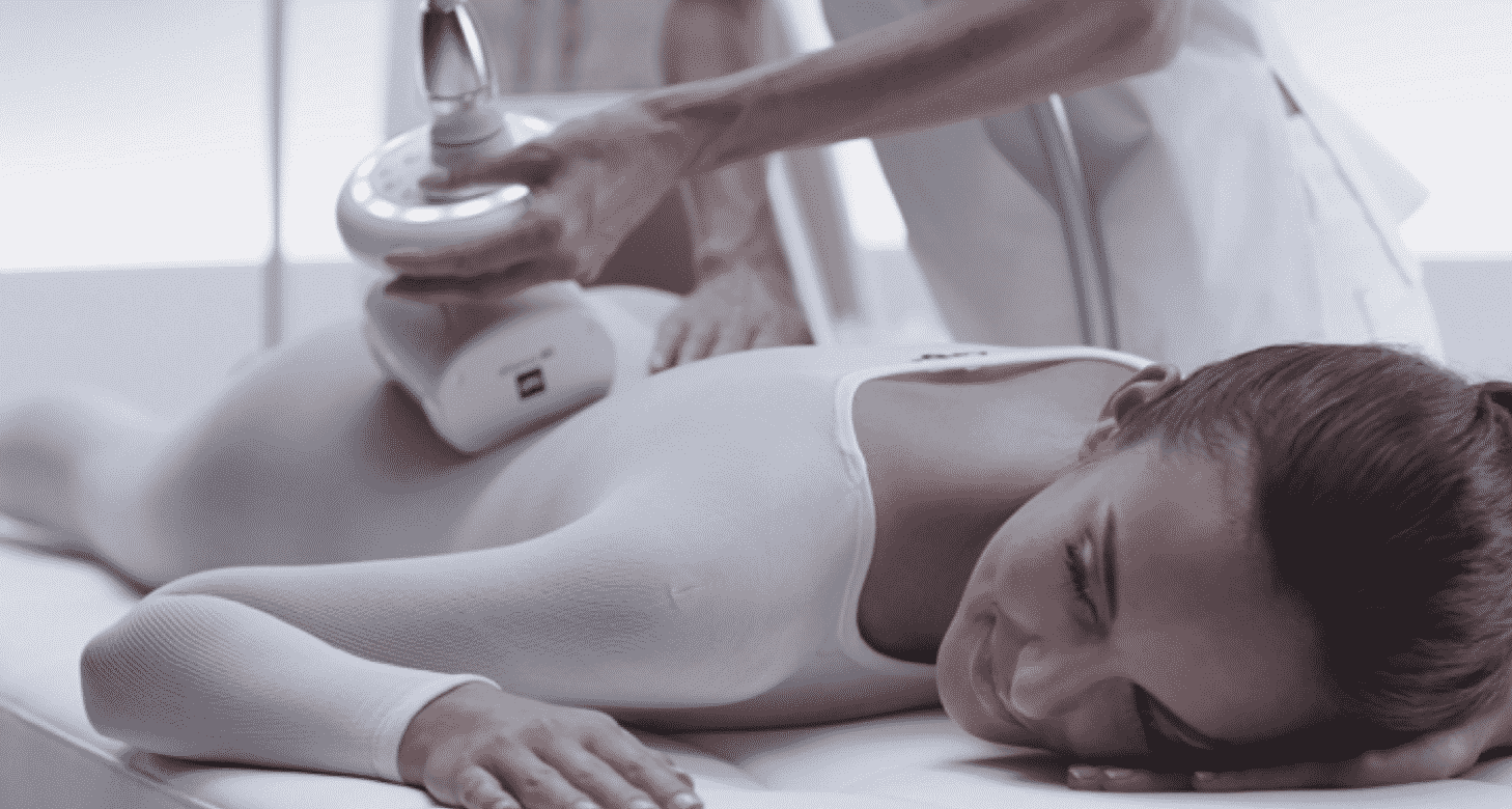 O femeie într-un body alb primește un tratament de remodelare corporală Endermologie Iași cu un dispozitiv portabil în timp ce stă întinsă pe o masă de tratament.