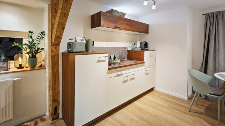 MainZauber Apartments früher MainTerrasse Miltenberg am Main - Erleben Sie den Inbegriff von Komfort und Stil in unserer luxuriösen Ferienwohnung, die perfekt darauf ausgelegt ist, Ihren Aufenthalt zu verschönern. Diese exquisite Unterkunft verfügt über eine moderne Küchenzeile mit eleganten weißen Schränken und edlen Holzakzenten, die mit allen wichtigen Geräten für mühelosen Komfort ausgestattet ist. Verbessern Sie Ihr kulinarisches Erlebnis in einem Raum, der durch natürliches Licht von Fenstervorhängen bereichert wird. Machen Sie es sich am eleganten Esstisch, umgeben von schicken weißen Stühlen, gemütlich, während Holzbalken und heller Holzboden der Wohnung Wärme und Charme verleihen. Ideal für alle, die eine erstklassige Ferienwohnung suchen, die modernen Komfort nahtlos mit einladender Ästhetik verbindet.