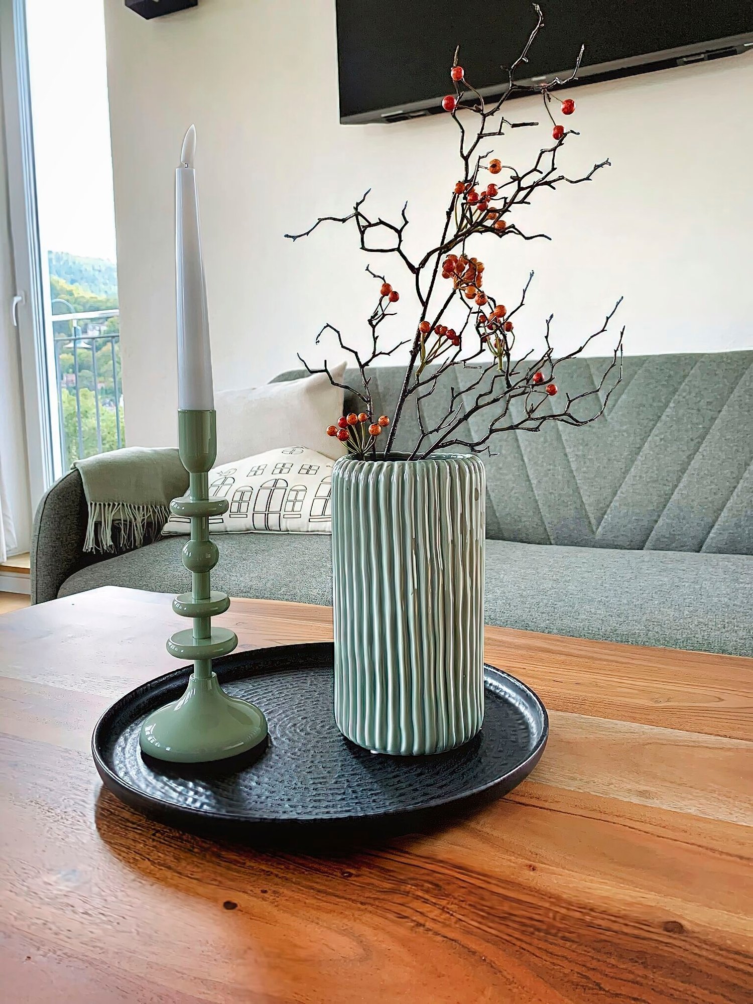 Entdecken Sie mit unseren luxuriösen Unterkünften das perfekte Urlaubsapartment. Dieser elegante Raum verfügt über ein modernes Wohnzimmer mit einem stilvollen Holztisch, der mit einer dekorativen Vase voller Zweige und roter Beeren geschmückt ist. Verbessern Sie Ihr Entspannungserlebnis mit der Atmosphäre eines grünen Kerzenständers mit einer weißen Kerze, alles elegant arrangiert auf einem eleganten schwarzen Tablett. Entspannen Sie sich auf dem plüschigen grauen Sofa, während natürliches Licht durch das große Fenster hereinströmt und eine einladende und ruhige Atmosphäre für Ihren Urlaubsort schafft. Egal, ob Sie Komfort oder Stil suchen, dieses luxuriöse Urlaubsapartment verspricht, Ihren Aufenthalt zu verbessern. - MainZauber Apartments Miltenberg am Main