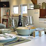 MainZauber Apartments Miltenberg am Main - Erleben Sie den ultimativen Komfort in dieser luxuriösen Ferienwohnung, in der ein gut gedeckter Esstisch die Mahlzeiten in eine elegante Angelegenheit verwandelt. Diese geräumige und gemütliche Wohnküche verfügt über elegante weiße Schränke und stilvolle Holzregale, die eine warme Atmosphäre schaffen, perfekt für Ihre Urlaubsunterkunftsbedürfnisse. Genießen Sie intime Abendessen mit grünen Schüsseln, einem Weinglas und einer Flasche Wein, ergänzt durch geschmackvolle Dekorationselemente. Ihre ideale Ferienwohnung erwartet Sie – buchen Sie jetzt, um sich während Ihres Urlaubs Entspannung und Eleganz zu gönnen.