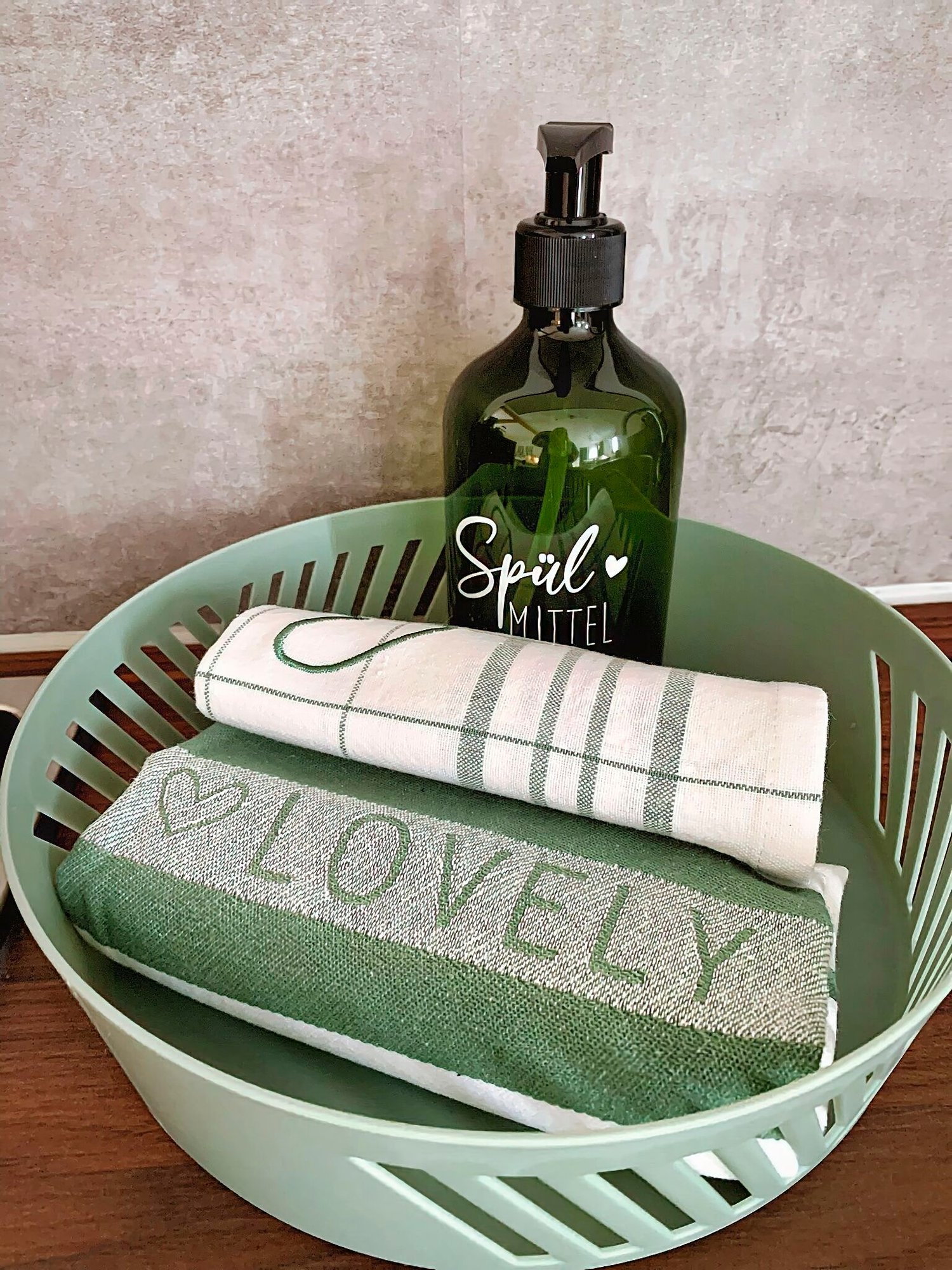Entdecken Sie die perfekte Ferienwohnung mit allem Komfort von zu Hause! Diese luxuriöse Unterkunft bietet Liebe zum Detail, wie einen charmanten grünen Korb, in dem sich zwei makellose Küchentücher befinden – eines mit dem fröhlichen Wort „LOVELY“ und ein anderes mit stilvollen Streifen. Eine grüne Pumpflasche mit der Aufschrift „Spülmittel“ steht bequem für Ihren Gebrauch bereit und verschönert Ihren Aufenthalt. Vor einer wunderschön gefliesten Wand machen diese durchdachten Details diese Ferienwohnung zur idealen Wahl für einen erholsamen Kurzurlaub. - MainZauber Apartments Miltenberg am Main