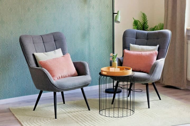 MainZauber Apartments früher MainTerrasse Miltenberg am Main - Luxuriöse Ferienwohnung in der Altstadt: Zwei graue Sessel, rosa-weiße Kissen, runder Tisch, Stehlampe, viel Grün.