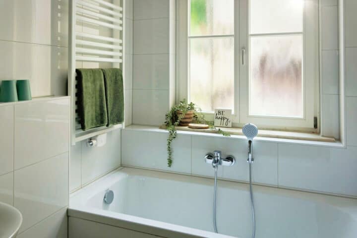 MainZauber Apartments früher MainTerrasse Miltenberg am Main - Modernes, weiß gefliestes Badezimmer in der Luxus-Ferienwohnung AltstadtZauber Miltenberg mit Badewanne, Fenster, Handtüchern.