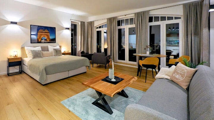 MainZauber Apartments früher MainTerrasse Miltenberg am Main - Entdecken Sie den perfekten Urlaubsort in diesem luxuriösen Apartment mit einem modernen und geräumigen Schlafzimmer. Genießen Sie eine erholsame Nachtruhe auf dem großen, bequemen Bett, ergänzt durch ein elegantes graues Sofa und einen eleganten Couchtisch aus Holz zum Entspannen. Die Unterkunft bietet einen einladenden kleinen Essbereich mit stilvollen Stühlen vor atemberaubenden raumhohen Fenstern mit schicken grauen Vorhängen, die einen atemberaubenden Ausblick bieten. Tauchen Sie ein in das künstlerische Ambiente mit sorgfältig kuratierten Kunstwerken an den Wänden. Glänzende Holzböden verleihen dem Raum Wärme, während sanfte Beleuchtung eine ruhige Atmosphäre für Ihren Urlaub schafft. Dieses Luxusapartment ist ideal für diejenigen, die erstklassige Ferienvermietungserlebnisse suchen, und wurde entworfen, um Ihren Aufenthalt unvergesslich zu machen.