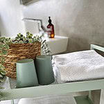 Entdecken Sie in unserer luxuriösen Ferienwohnung einen ruhigen und Spa-ähnlichen Rückzugsort, perfekt für Ihren nächsten Kurzurlaub. Stellen Sie sich vor, Sie entspannen sich in einem elegant gestalteten Badezimmer mit einem stilvollen grünen Metallwagen, der mit tadellos gefalteten weißen Handtüchern bestückt ist. Für zusätzlichen Komfort finden Sie zwei bezaubernde grüne Tassen und einen geflochtenen Korb, der mit erfrischendem Grün geschmückt ist. Beachten Sie im sanft verschwommenen Hintergrund das glatte Waschbecken und die elegante braune Flasche, die das ruhige Ambiente dieser exquisiten Unterkunft unterstreichen. Gönnen Sie sich das ultimative Entspannungserlebnis, wenn Sie diese außergewöhnliche Ferienwohnung für Ihren Aufenthalt buchen. - MainZauber Apartments Miltenberg am Main