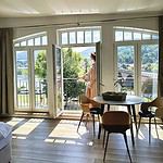 Stellen Sie sich vor, Sie stehen auf dem Balkon einer luxuriösen Ferienwohnung und genießen die atemberaubende Aussicht auf einen ruhigen Fluss und sanfte Hügel. Diese stilvolle Unterkunft verfügt über große Fenster, die einen atemberaubenden Panoramablick bieten und natürliches Licht in das gemütliche Interieur bringen. Genießen Sie köstliche Mahlzeiten an Ihrem runden Esstisch mit vier bequemen Stühlen, alles vor eleganten Hartholzböden. Genießen Sie die perfekte Mischung aus Komfort und Ruhe in Ihrem Traumurlaubsort. - MainZauber Apartments Miltenberg am Main