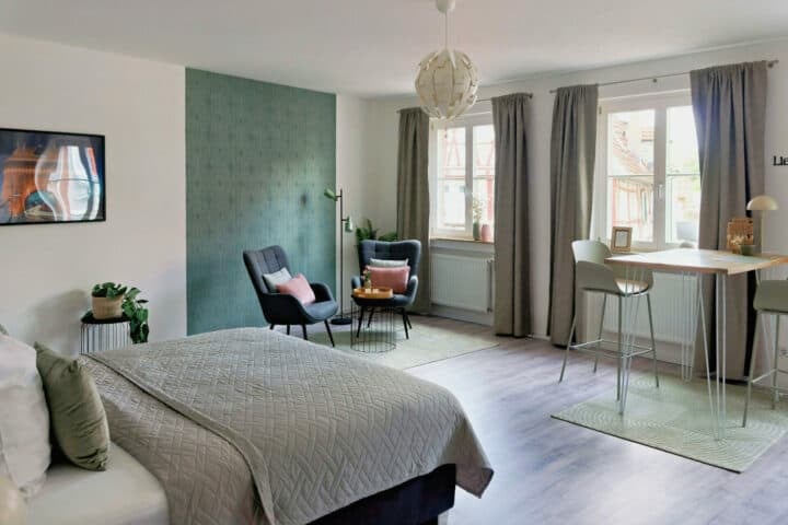 MainZauber Apartments früher MainTerrasse Miltenberg am Main - Luxuriöse Ferienwohnung in der Altstadt: Modernes Studio, großes Fenster, stilvolle Sitzgruppe, Esstisch & gemütliches Bett.
