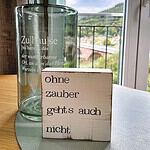 Suchen Sie die perfekte Ferienwohnung? Entdecken Sie unvergleichlichen Luxus in unseren erstklassigen Unterkünften, in denen jedes Detail darauf ausgelegt ist, Ihren Urlaub zu verschönern. Stellen Sie sich vor, Sie entspannen sich in einem wunderschön eingerichteten Luxusapartment für den Urlaub mit atemberaubender Aussicht auf üppige Bäume und sanfte Hügel, eingerahmt von großen Fenstern. Erfreuen Sie sich an einzigartigen Dekorelementen wie einer Glasvase und charmanten Holzklötzen mit Sprüchen wie „Ohne Zauber geht’s auch nicht“, die Ihrem Aufenthalt einen Hauch von Zauber verleihen. Ihr Traumurlaub erwartet Sie in unseren außergewöhnlichen Unterkünften! - MainZauber Apartments Miltenberg am Main