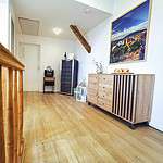 Treten Sie ein in die Ferienwohnung Ihrer Träume, wo Sie ein moderner und heller Flur mit einer eleganten Holztreppe und einem schicken Sideboard begrüßt. Dieser exquisite Raum, der sich perfekt für Ihren Luxusapartmenturlaub eignet, verfügt über einen praktischen Weinkühlschrank, der Ihren Aufenthalt noch schöner macht. Die makellos weiße Wand ziert ein atemberaubendes Landschaftskunstwerk, begleitet von einer stilvollen Anordnung frischer Blumen in einer Vase und einer Schale mit Äpfeln auf dem Sideboard – jedes Detail ist für eine unvergessliche Urlaubsunterkunft konzipiert. - MainZauber Apartments Miltenberg am Main