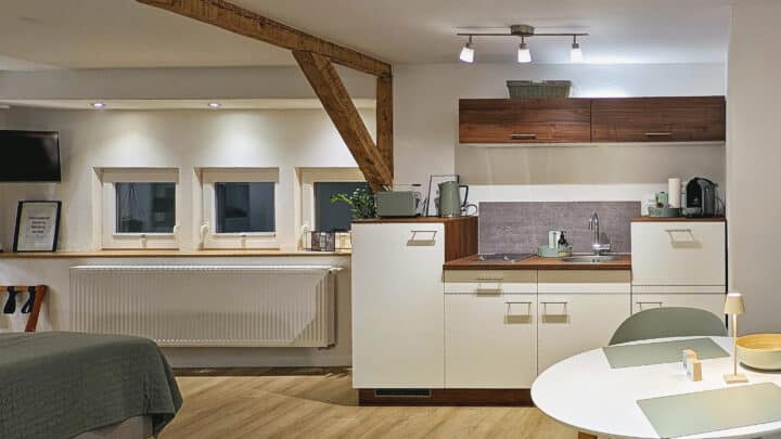 MainZauber Apartments früher MainTerrasse Miltenberg am Main - Entdecken Sie in diesem luxuriösen Studio die perfekte Ferienwohnung für Ihren Urlaub. Diese Unterkunft bietet eine hervorragende Mischung aus Komfort und Bequemlichkeit und verfügt über eine sorgfältig gestaltete Küchenzeile mit eleganten Holzschränken, einer kompakten Spüle und modernen Geräten, die ideal für alle Ihre kulinarischen Bedürfnisse sind. Entspannen Sie sich am charmanten runden Tisch mit Stühlen oder entspannen Sie sich auf dem ordentlich gemachten Bett. Die freiliegenden Holzbalken und die sanfte Beleuchtung tragen zu einer einladenden Atmosphäre bei, die sowohl Entspannung als auch Stil während Ihres Aufenthalts in diesem luxuriösen Urlaubsapartment verspricht.