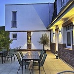 MainZauber Apartments Miltenberg am Main - Entdecken Sie mit dieser atemberaubenden Luxusunterkunft Ihre Traumferienwohnung. Stellen Sie sich vor, Sie genießen einen ruhigen Abend auf einer modernen Terrasse mit stilvollen Tischen und Stühlen, alles vor der Kulisse eines makellos weißen Gebäudes in der Abenddämmerung. Diese Ferienwohnung bietet eine idyllische Atmosphäre mit wunderschön beleuchteten Bereichen, die perfekt zum Entspannen geeignet sind. Ein schicker Sonnenschirm steht elegant neben einem üppigen Baum und verstärkt die ruhige Atmosphäre. Genießen Sie die atemberaubende Aussicht auf sattes Grün und sanfte Hügel unter einem klaren blauen Himmel, der dies zum idealen Ort für Ihren perfekten Urlaub macht.