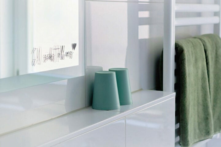 MainZauber Apartments früher MainTerrasse Miltenberg am Main - Zwei grüne Becher stehen kopfüber auf dem weißen Bad-Tresen dieser luxuriösen Altstadt Ferienwohnung mit Spiegel und Handtuch.