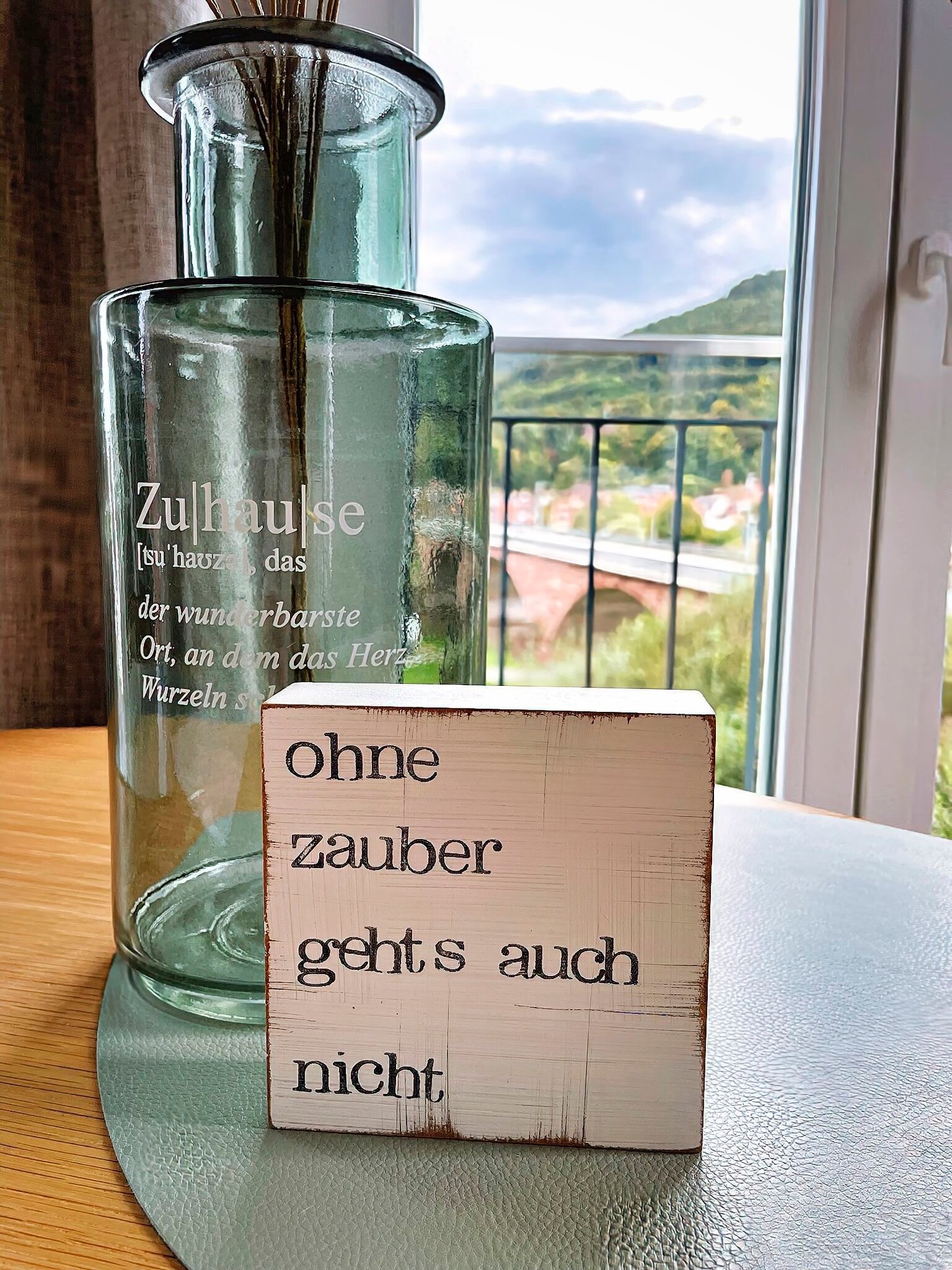 Suchen Sie die perfekte Ferienwohnung? Entdecken Sie unvergleichlichen Luxus in unseren erstklassigen Unterkünften, in denen jedes Detail darauf ausgelegt ist, Ihren Urlaub zu verschönern. Stellen Sie sich vor, Sie entspannen sich in einem wunderschön eingerichteten Luxusapartment für den Urlaub mit atemberaubender Aussicht auf üppige Bäume und sanfte Hügel, eingerahmt von großen Fenstern. Erfreuen Sie sich an einzigartigen Dekorelementen wie einer Glasvase und charmanten Holzklötzen mit Sprüchen wie „Ohne Zauber geht’s auch nicht“, die Ihrem Aufenthalt einen Hauch von Zauber verleihen. Ihr Traumurlaub erwartet Sie in unseren außergewöhnlichen Unterkünften! - MainZauber Apartments Miltenberg am Main
