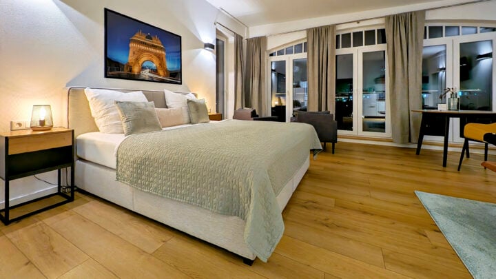 MainZauber Apartments früher MainTerrasse Miltenberg am Main - Entdecken Sie Ihre ideale Ferienwohnung, die die perfekte Mischung aus Komfort und Stil bietet. Diese luxuriöse Unterkunft verfügt über ein geräumiges Schlafzimmer mit einem weichen Bett mit einer eleganten grünen Bettdecke, das erholsame Nächte verspricht. Genießen Sie die Kunstfertigkeit über dem Bett und entspannen Sie sich im sanften Schein einer Lampe auf einem eleganten Nachttisch aus Holz. Die Wohnung verfügt über schöne Holzböden und große Fenster mit stilvollen Vorhängen, die Ihren Aufenthalt verschönern. Entspannen Sie sich im durchdacht gestalteten Sitzbereich und machen Sie diese Luxuswohnung zu Ihrem perfekten Rückzugsort für ein exquisites Urlaubserlebnis.