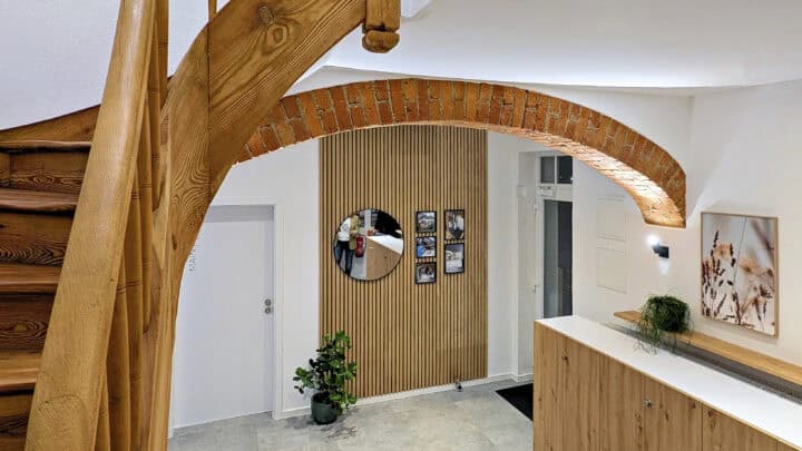 MainZauber Apartments früher MainTerrasse Miltenberg am Main - Entdecken Sie eine atemberaubende Luxus-Ferienwohnung, perfekt für Ihren nächsten Urlaub. Diese exquisite Unterkunft verfügt über ein modernes Interieur mit einzigartigen Merkmalen, die ihren Charme unterstreichen. Bewundern Sie die wunderschöne geschwungene Holztreppe, die nahtlos mit einem eleganten Ziegelbogen gepaart ist und einen herrlichen Hauch von Raffinesse verleiht. Die Wände sind geschmackvoll mit einem runden Spiegel und gerahmten Kunstwerken dekoriert, die das stilvolle Ambiente unter dem Holzlamellendesign unterstreichen. Eine üppige Pflanze neben der makellos weißen Tür wertet diesen einladenden Raum auf, während eine elegante, mit Grünpflanzen geschmückte Holztheke einen idealen Ort zum Entspannen oder für Unterhaltung bietet. Erleben Sie noch heute unvergleichlichen Komfort und Eleganz in Ihrer Traumferienwohnung!