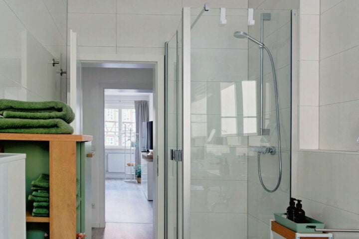 MainZauber Apartments früher MainTerrasse Miltenberg am Main - Modernes Bad in Luxus Ferienwohnung mit Glasdusche, Holzbord, grünen Handtüchern und Blick ins helle Wohnzimmer der Unterkunft.