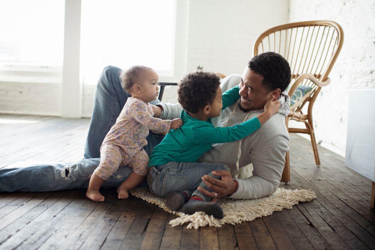 father laying on floor playing with his two children