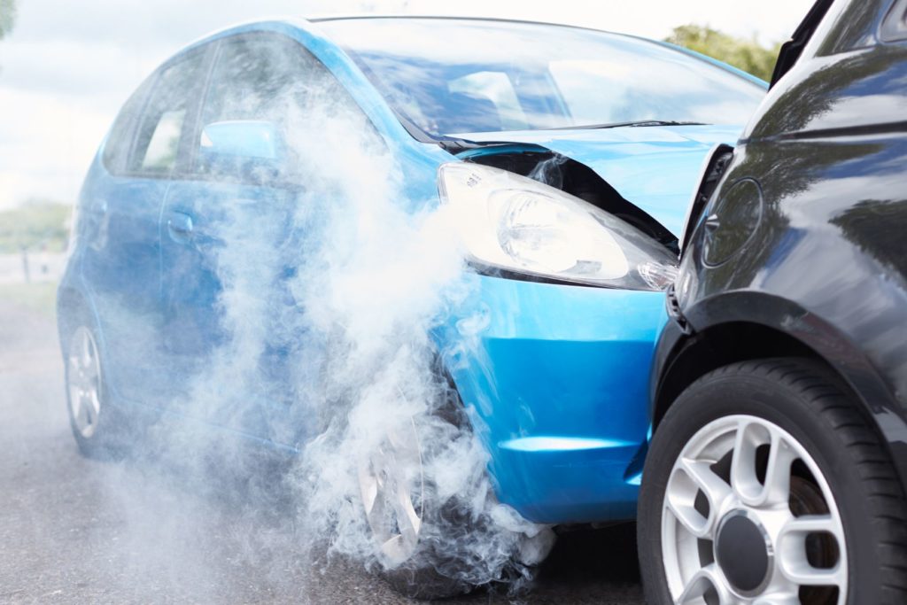A car accident involving a blue car and black car with smoke from the collision