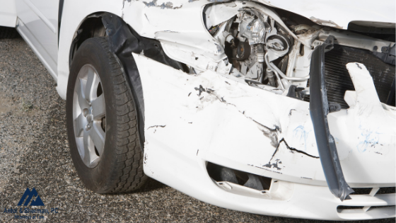 Close up of the front of a white sedan with recent front end damage from a car accident.