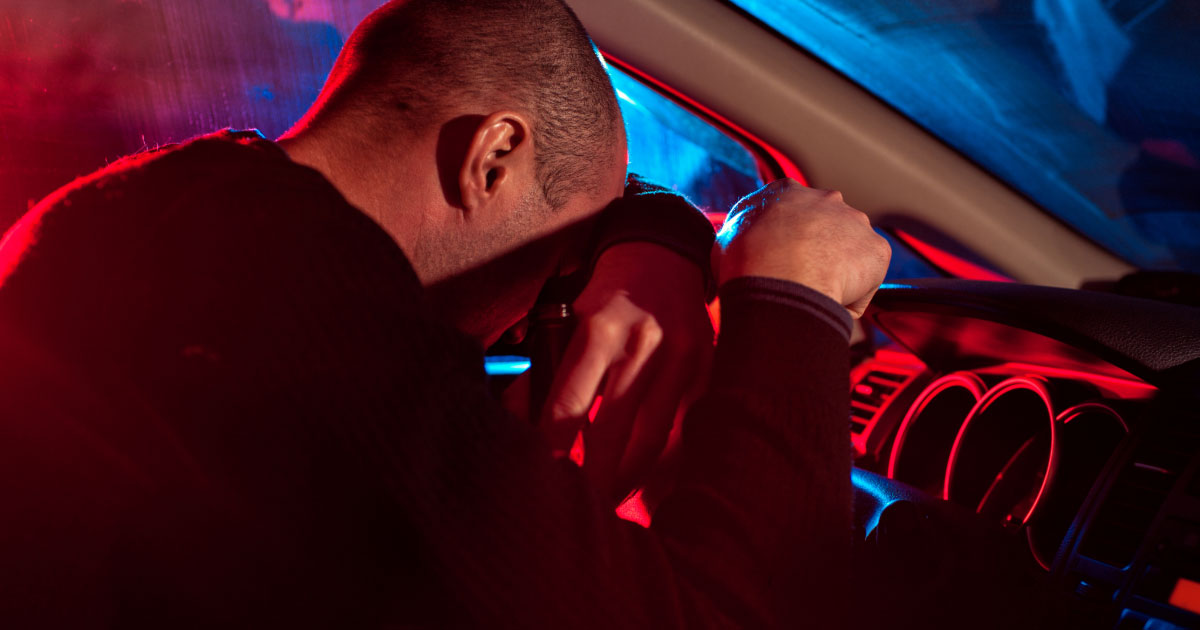 Man resting his head on steering wheel because he's too drunk to drive